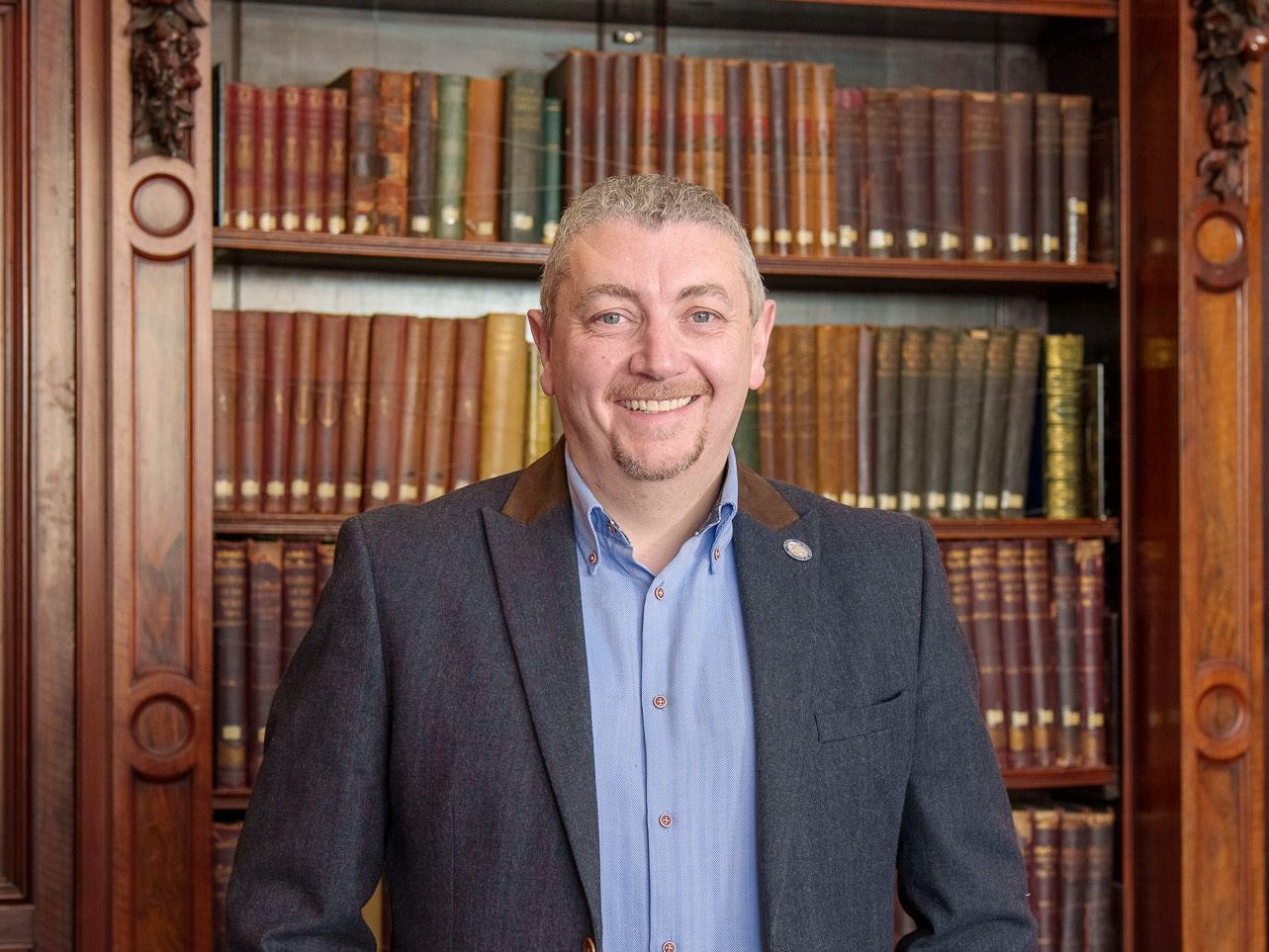 Neil Ellis standing in front of the library books in the Members' Library