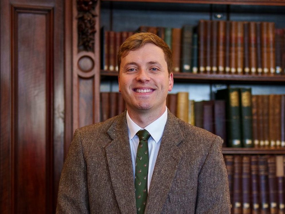 Christian Stelfox standing in front of the library books in the Members' Library